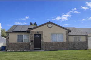 Ranch-style house with stone siding, solar panels, stucco siding, and a front yard