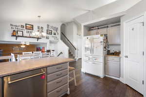Kitchen with stainless steel dishwasher, white refrigerator with ice dispenser, gray cabinets, light countertops, and dark wood-style floors