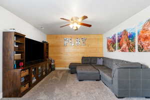 Living room featuring wood walls, carpet floors, and ceiling fan