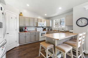 Kitchen featuring white appliances, light countertops, a breakfast bar area, a peninsula, and lofted ceiling
