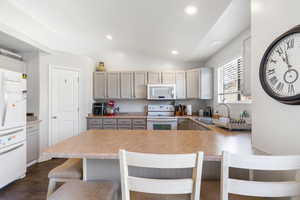 Kitchen featuring a kitchen bar, white appliances, gray cabinetry, light countertops, and lofted ceiling