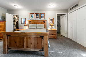 Bedroom with a textured ceiling, dark carpet, and a spacious closet