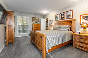 Bedroom with a textured ceiling, dark colored carpet, and a spacious closet