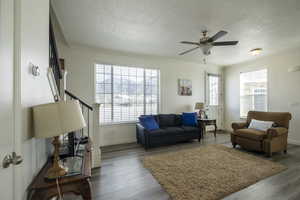Living room with wood finished floors, a ceiling fan, a textured ceiling, and healthy amount of natural light
