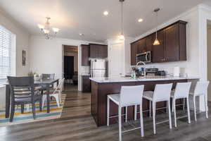 Kitchen with dark wood finish cabinetry, a peninsula, stainless steel appliances, ornamental molding, and dark wood finished floors