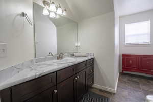 Bathroom featuring vanity, stone finish flooring, and lofted ceiling