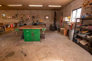 Misc room featuring concrete block wall, concrete floors, a workshop area, and a wood stove