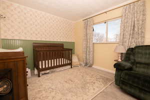 Bedroom featuring wallpapered walls, ornamental molding, light colored carpet, a nursery area, and a wainscoted wall