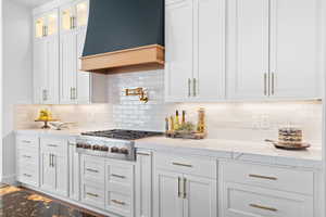 Kitchen with light stone countertops, white cabinets, stainless steel gas cooktop, and glass insert cabinets