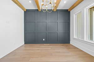 Unfurnished dining area featuring a decorative wall, beam ceiling, hanging lights, and light wood finished floors