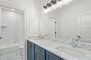 Bathroom with double vanity, light marble finish floors, and bathtub / shower combination