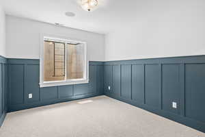 Unfurnished room featuring a decorative wall, wainscoting, and carpet floors