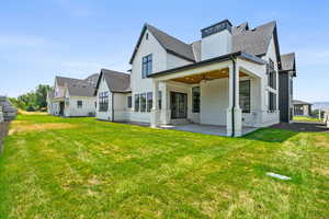 Back of house featuring a ceiling fan, a shingled roof, a patio area, and a lawn