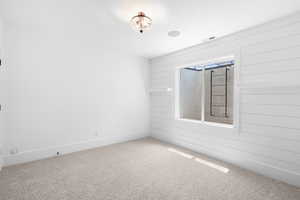 Carpeted empty room featuring wood walls and baseboards
