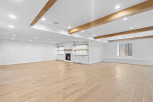 Unfurnished living room with recessed lighting, a warm lit fireplace, light wood finished floors, and beam ceiling