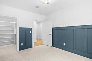 Unfurnished bedroom featuring a decorative wall, a walk in closet, wainscoting, and carpet flooring