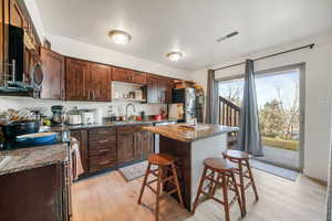Kitchen with dark wood finish cabinetry, dark stone countertops, stainless steel appliances, a kitchen island, and a breakfast bar