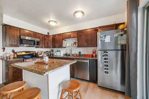 Kitchen featuring stainless steel appliances, dark stone counters, a center island, light wood-type flooring, and a breakfast bar area