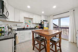 Kitchen featuring stainless steel appliances, white cabinets, light wood-style floors, dark stone countertops, and recessed lighting
