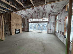 Unfurnished living room with concrete flooring, a high ceiling, and a fireplace