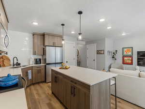 Kitchen featuring a kitchen island, stainless steel appliances, decorative light fixtures, light wood-type flooring, and open floor plan
