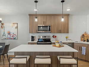 Kitchen featuring a breakfast bar, a kitchen island, stainless steel appliances, light wood-type flooring, and hanging light fixtures