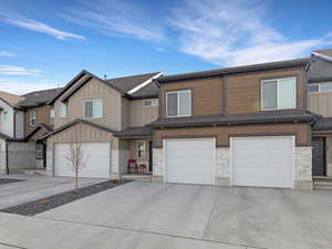 View of front facade with board and batten siding, stone siding, an attached garage, and driveway