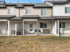 Rear view of house featuring a yard, a patio, stone siding, and roof with shingles