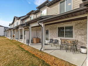 Rear view of property featuring a patio, stone siding, and a yard