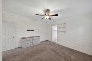 Unfurnished bedroom featuring brick wall, carpet, ceiling fan, and a textured ceiling