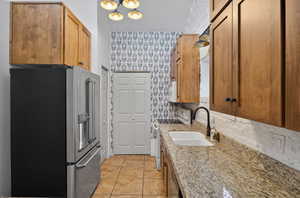 Kitchen with high end fridge, white electric stove, light stone countertops, wallpapered walls, and light tile patterned floors