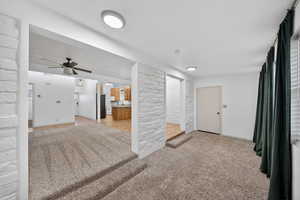 Unfurnished living room with a textured ceiling, light carpet, brick wall, and ceiling fan