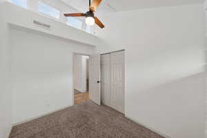 Unfurnished bedroom featuring a high ceiling, carpet flooring, a ceiling fan, and a closet
