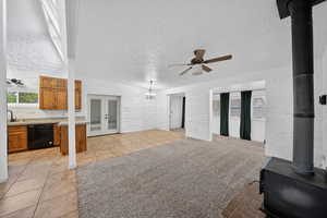 Unfurnished living room featuring a ceiling fan, a textured ceiling, brick wall, a wood stove, and french doors