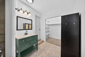 Bathroom with a walk in closet, vanity, a textured ceiling, light tile patterned flooring, and light colored carpet