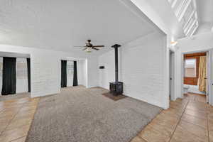 Unfurnished living room with light carpet, light tile patterned floors, brick wall, a wood stove, and a textured ceiling