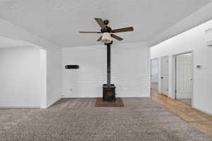 Unfurnished living room with carpet floors, brick wall, a textured ceiling, a wood stove, and a ceiling fan
