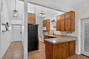 Kitchen with wood finish cabinetry, white appliances, light stone countertops, a peninsula, and light tile patterned flooring