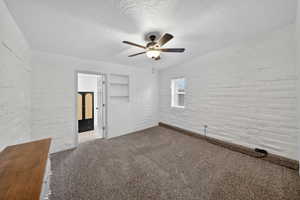 Unfurnished bedroom with brick wall, carpet, ceiling fan, and a textured ceiling