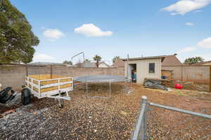 Fenced backyard featuring a trampoline and an outdoor structure
