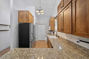 Kitchen featuring high quality fridge, light stone countertops, hanging light fixtures, wood finish cabinets, and wallpapered walls
