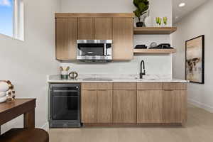 Kitchen with modern cabinets, wine cooler, open shelves, light stone counters, and stainless steel microwave