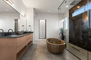Full bath with double vanity, a marble finish shower, a spacious closet, a soaking tub, and dark tile patterned floors