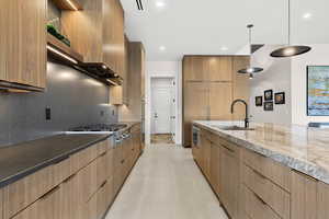 Kitchen featuring modern cabinets, dark stone countertops, hanging light fixtures, and stainless steel appliances