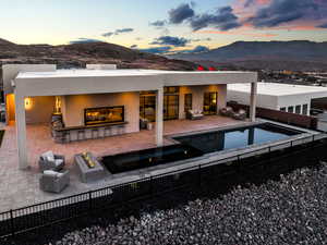 Back of house at dusk with a mountain view, stucco siding, an outdoor fire pit, an outdoor lounge area with bar, and a patio area