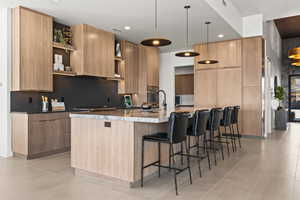 Kitchen featuring modern cabinets, a large island, a kitchen bar, hanging light fixtures, and dark stone countertops