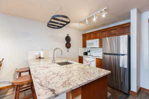 Kitchen with a breakfast bar area, white appliances, a peninsula, track lighting, and light stone countertops