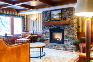 Living room featuring coffered ceiling, a stone fireplace, and wooden walls