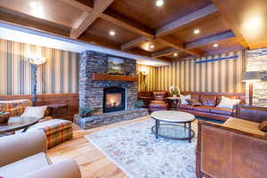 Living room with wallpapered walls, a stone fireplace, wood-type flooring, beamed ceiling, and recessed lighting