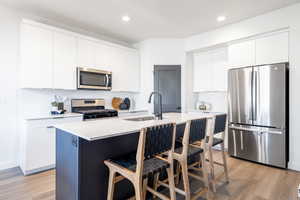 Kitchen featuring stainless steel appliances, a breakfast bar, a center island with sink, light wood-type flooring, and white cabinets